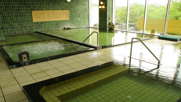 A large indoor swimming pool with multiple lanes, a tiled floor, and a green-tiled wall.