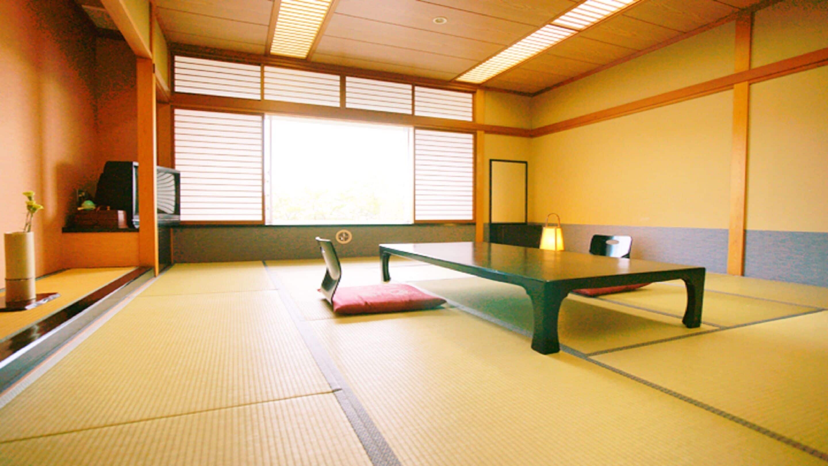 A tatami mat room with a low table, a cushion, a small shelf with a vase, and a window with blinds.