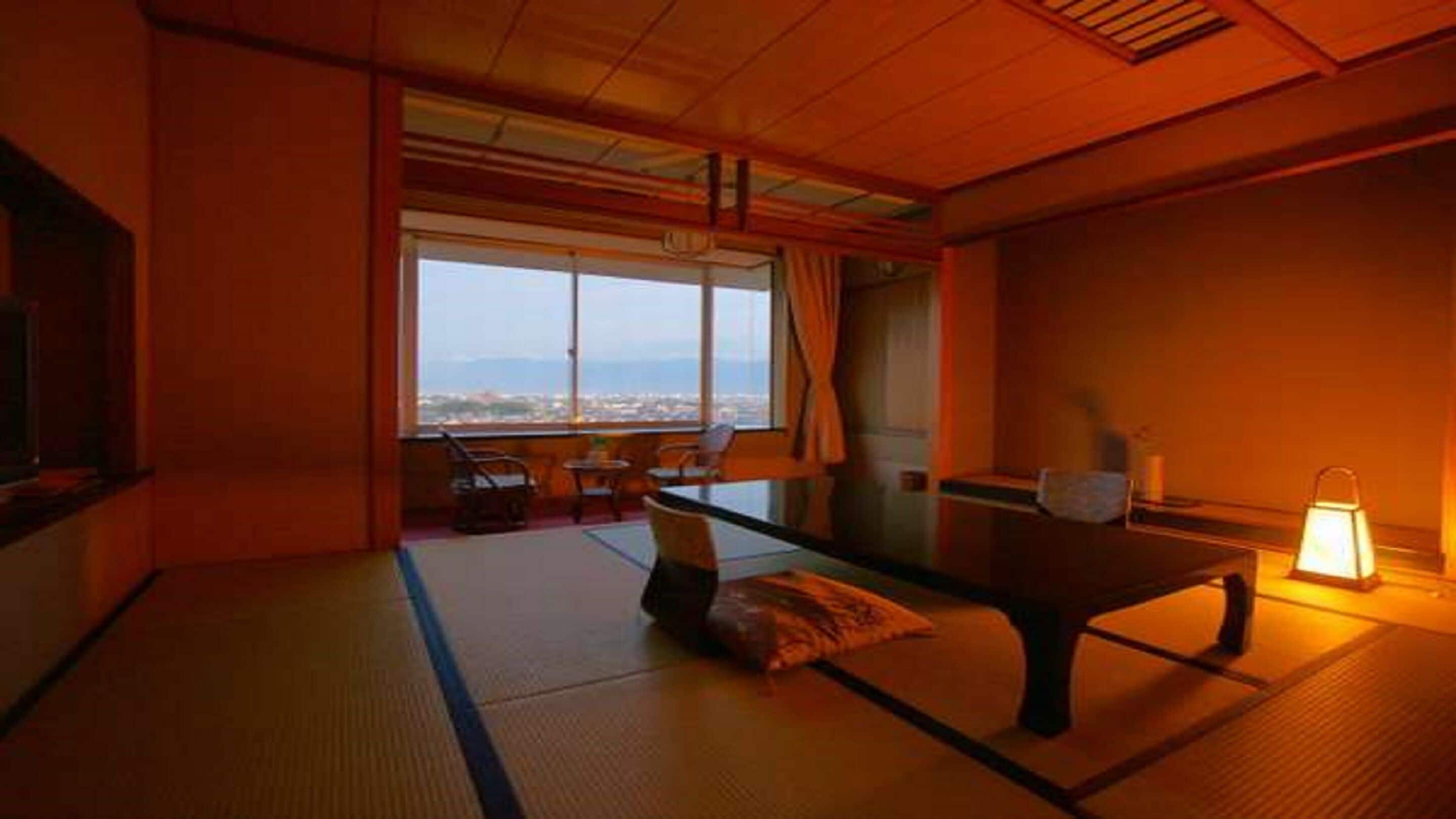 A traditional Japanese room with tatami flooring, a low table, and a view of a cityscape through large windows.