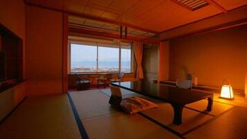 A traditional Japanese room with tatami flooring, a low table, and a view of a cityscape through large windows.