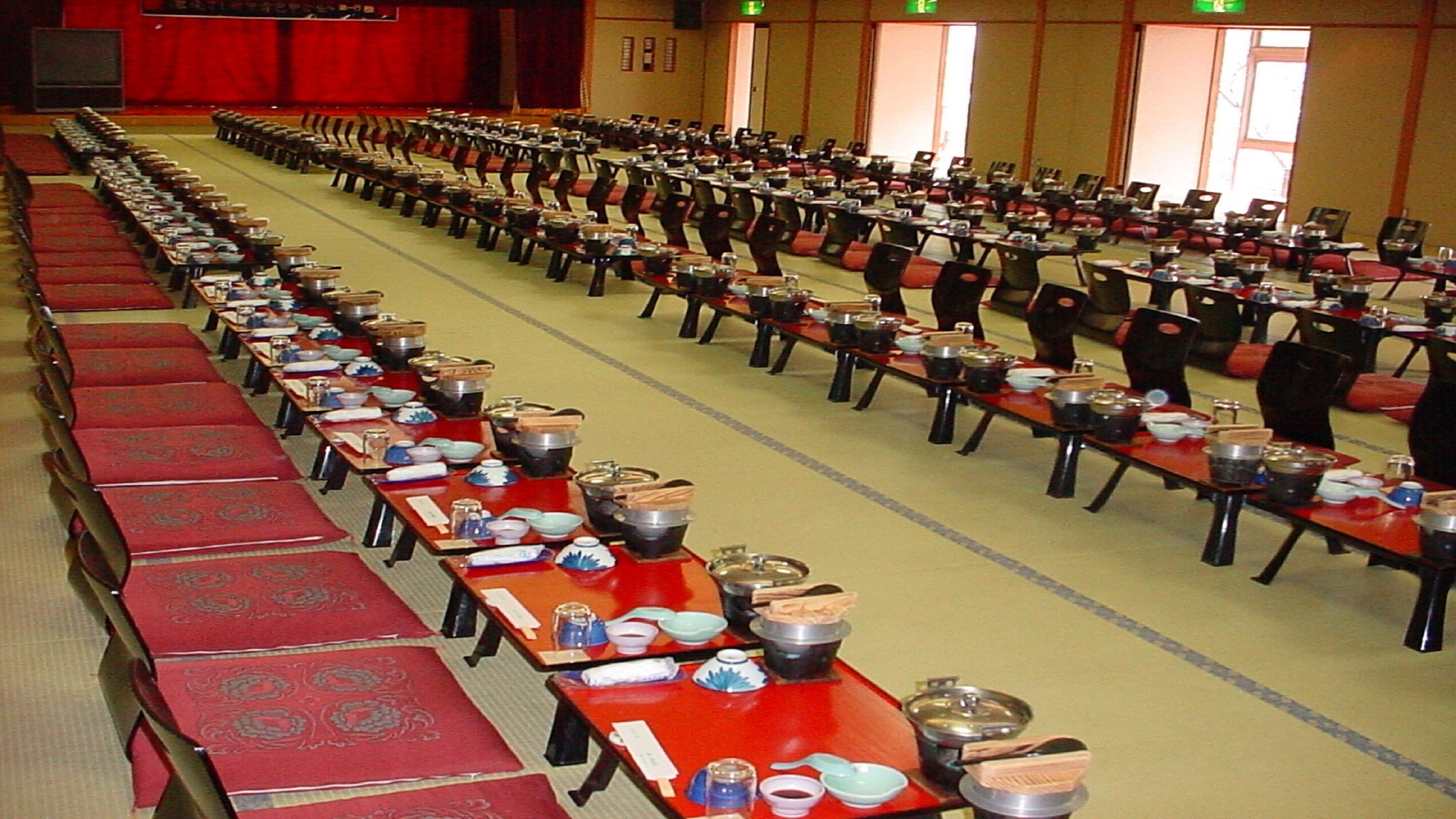 Un amplio salón de banquetes con filas de mesas dispuestas para un evento formal.
