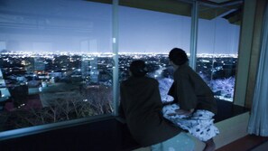 Dos personas sentadas junto a un amplio ventanal con vistas a la ciudad de noche.