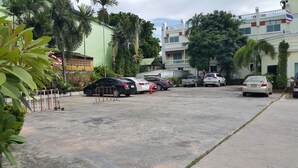 A parking area with several cars, a green building, and a white building with a flag. - Windmill Resort Hotel (Pattaya)