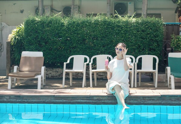 A poolside area with a person sitting on a chair, a pool, and a hedge in the background.