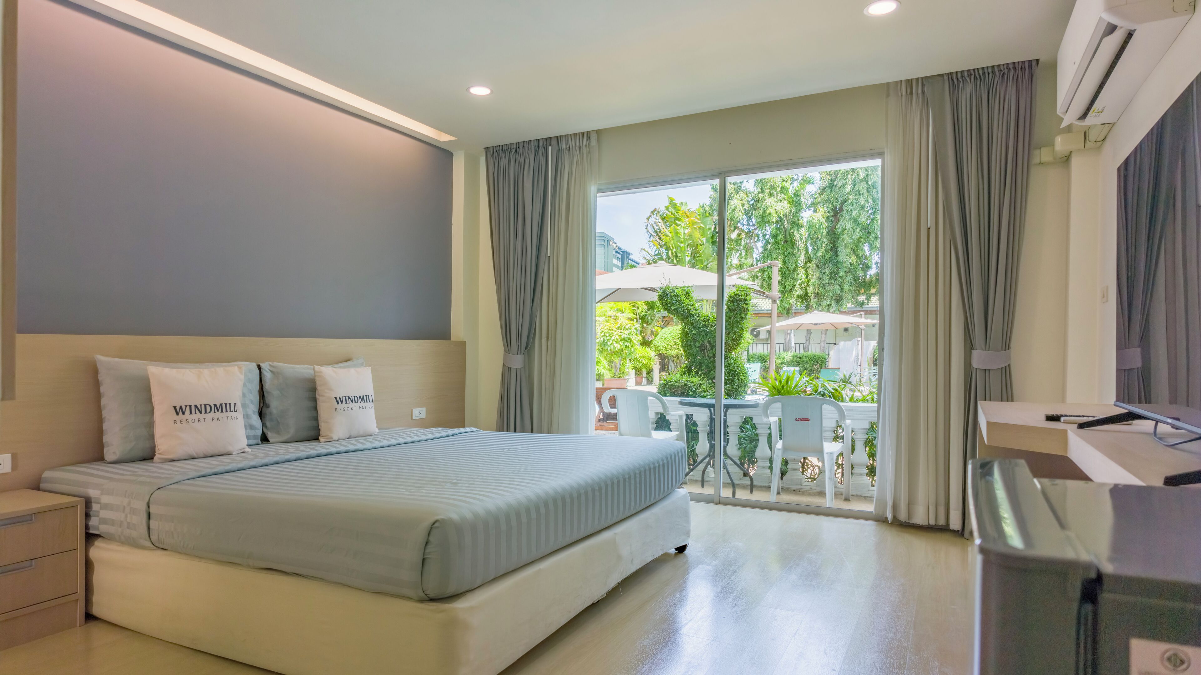 Habitación de hotel con cama, mesitas de noche, escritorio con computadora y vista al exterior.