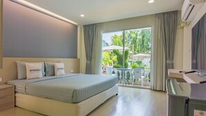 A hotel room with a bed, bedside tables, a desk with a computer, and a view of the outdoor area. - Windmill Resort Hotel (Pattaya)