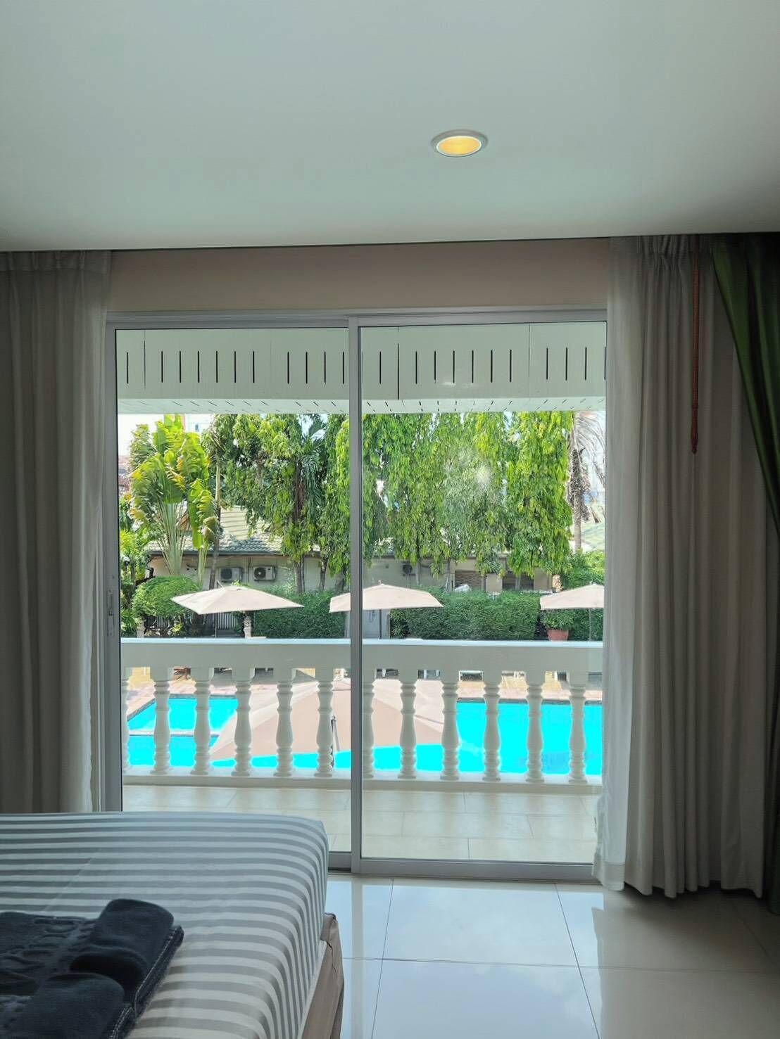 A hotel room with a bed, a view of a swimming pool, and a balcony with a railing.