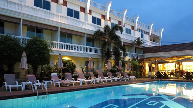 A hotel pool area with lounge chairs and umbrellas, a swimming pool with blue tiles, and a multi-story building with balconies. - Windmill Resort Hotel (Pattaya)