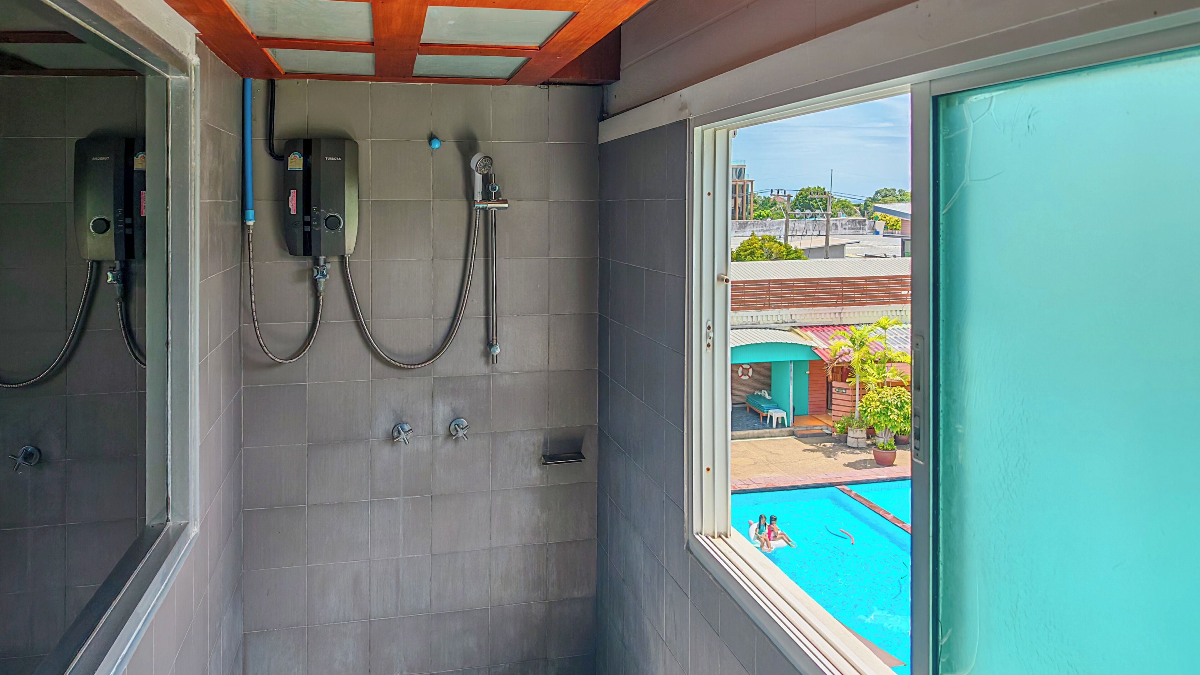 Baño con baldosas grises, ducha y ventana con vistas a una piscina.