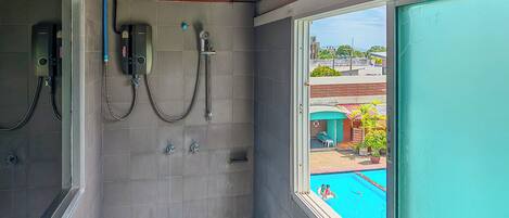 Baño con baldosas grises, ducha y ventana con vistas a una piscina.