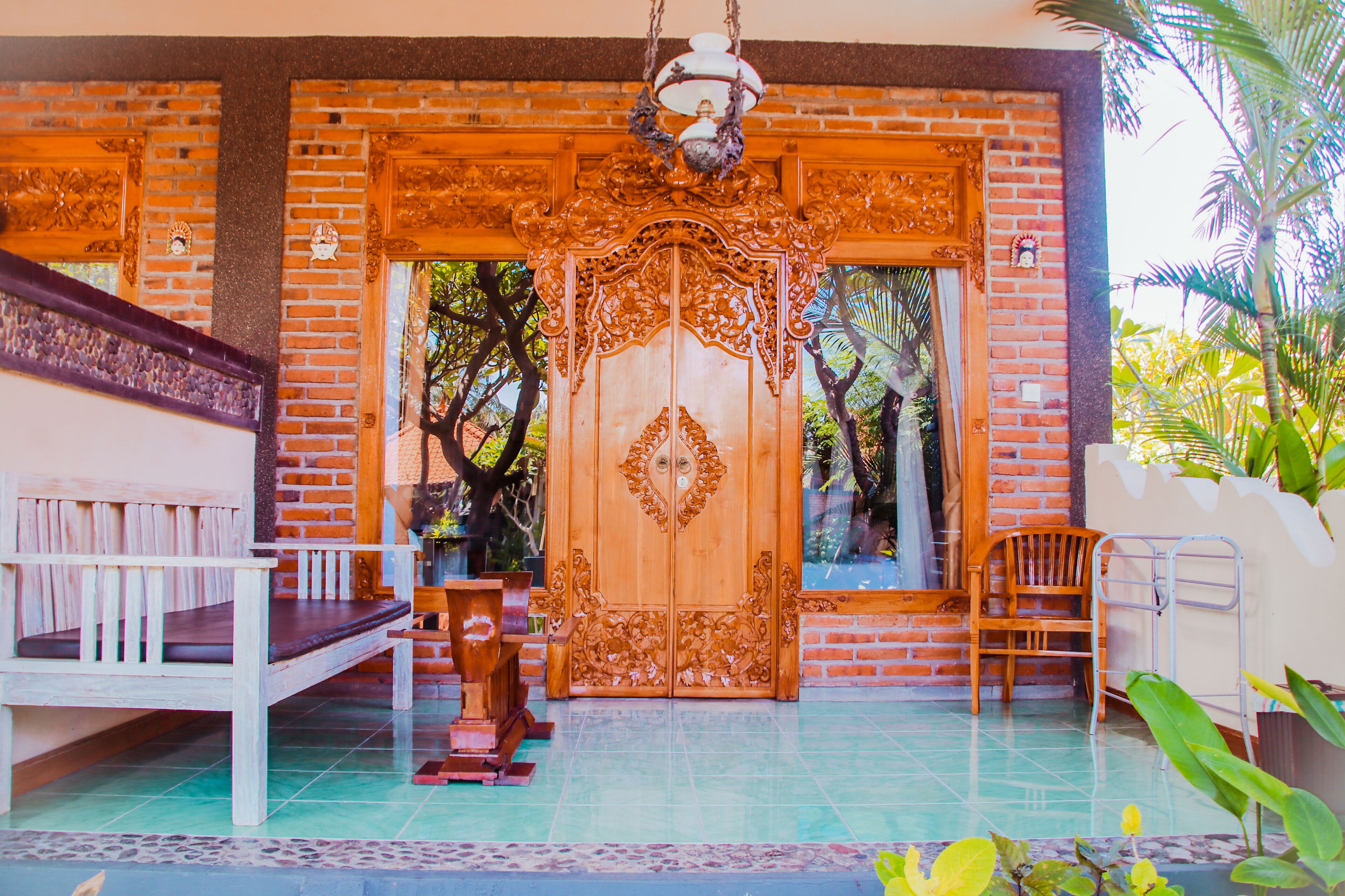 Una puerta de madera con elaborados adornos, un banco y una silla frente a un edificio con suelo de baldosas.