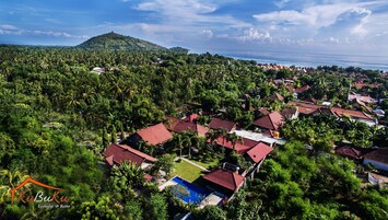 Vista aérea de un resort con varias edificaciones, una piscina y abundante vegetación.