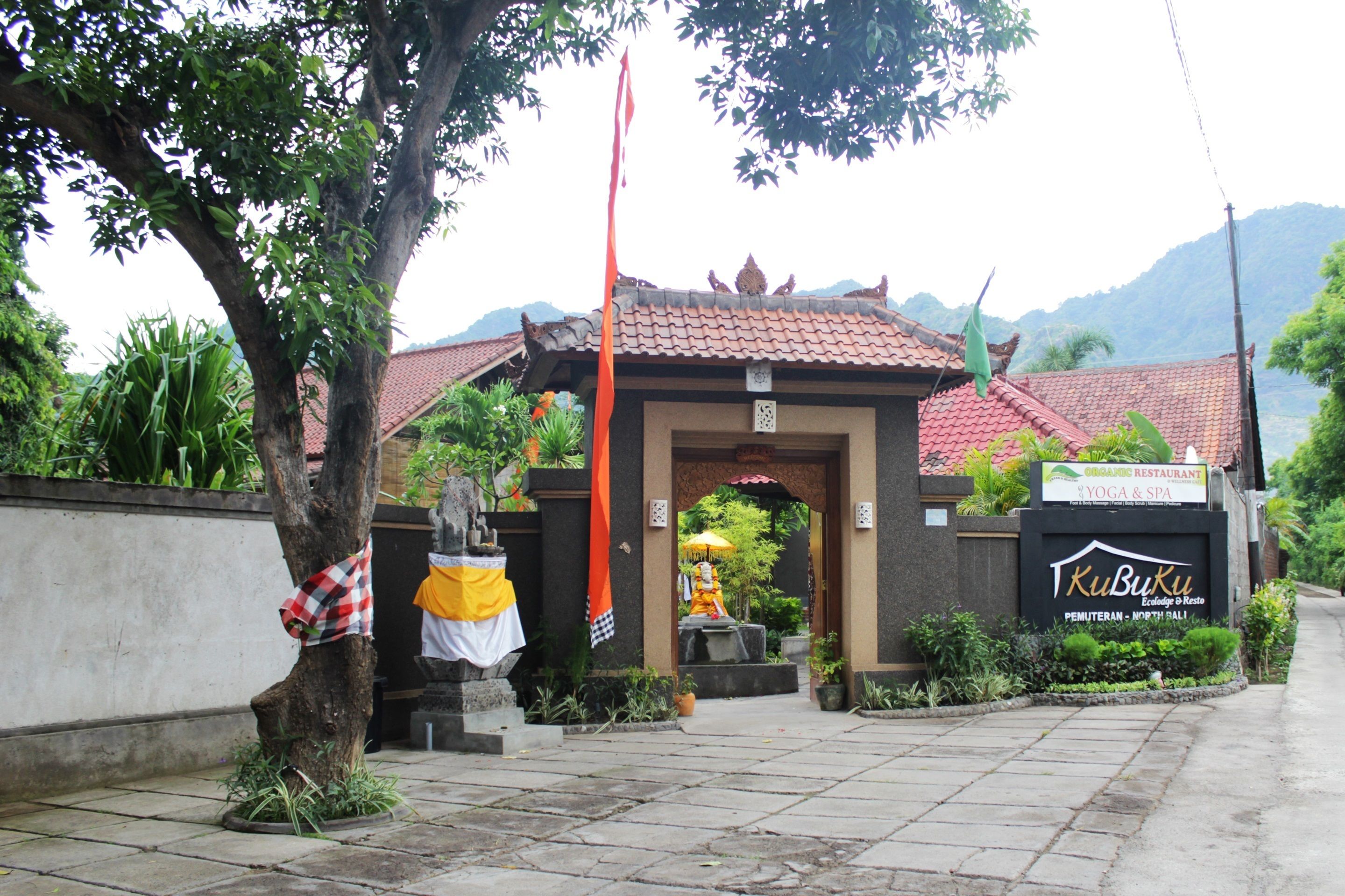 A traditional building with a tiled roof, a signboard for a restaurant and yoga & spa, and a statue in the entrance.