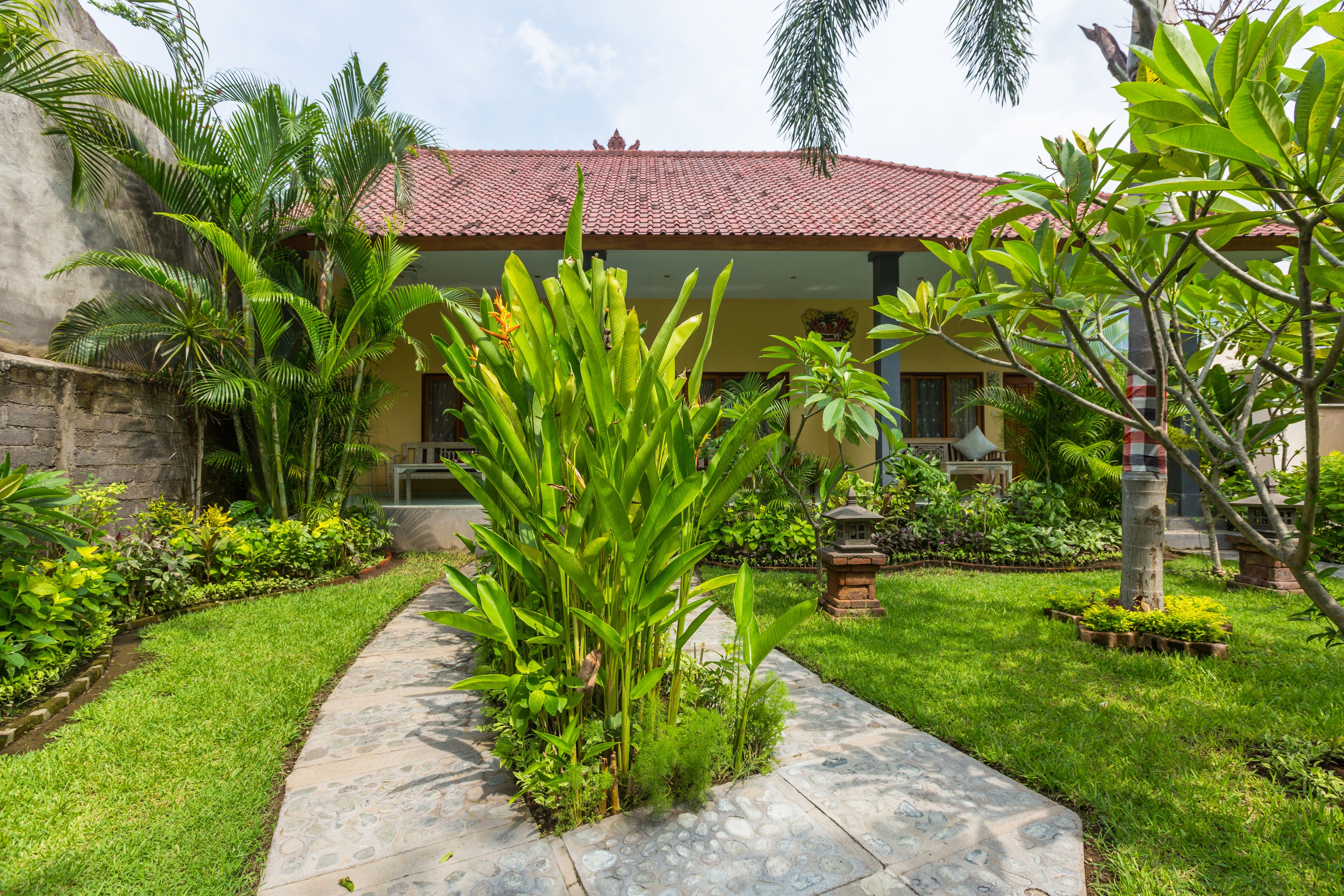 A well-maintained garden with a stone pathway leading to a building with a red-tiled roof.