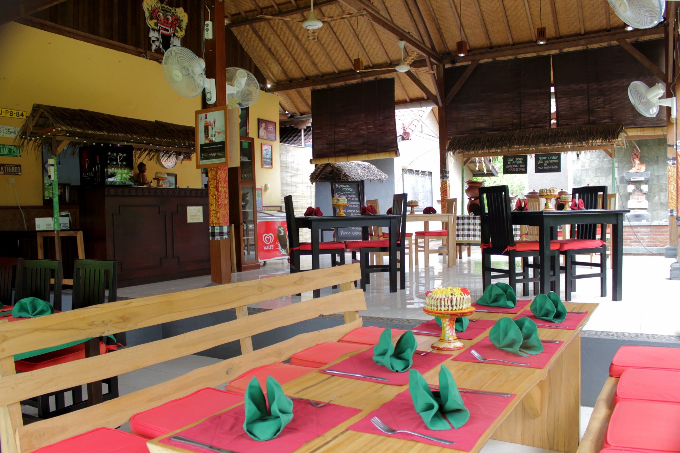 A restaurant with wooden tables and benches, red cushions, and a thatched roof.