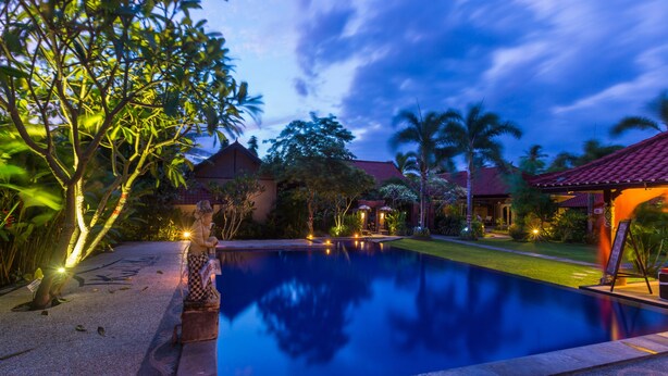 A swimming pool with a surrounding garden and a building with a red roof.