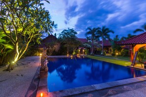A swimming pool with a surrounding garden and a building with a red roof.