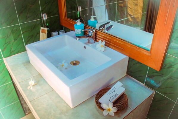 A bathroom with a white sink, green tiles, a mirror, and toiletries.