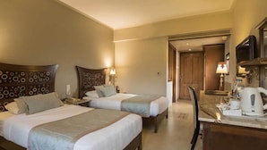 Quarto de hotel com duas camas, uma escrivaninha, uma cadeira, uma televisão e um aparelho de café.