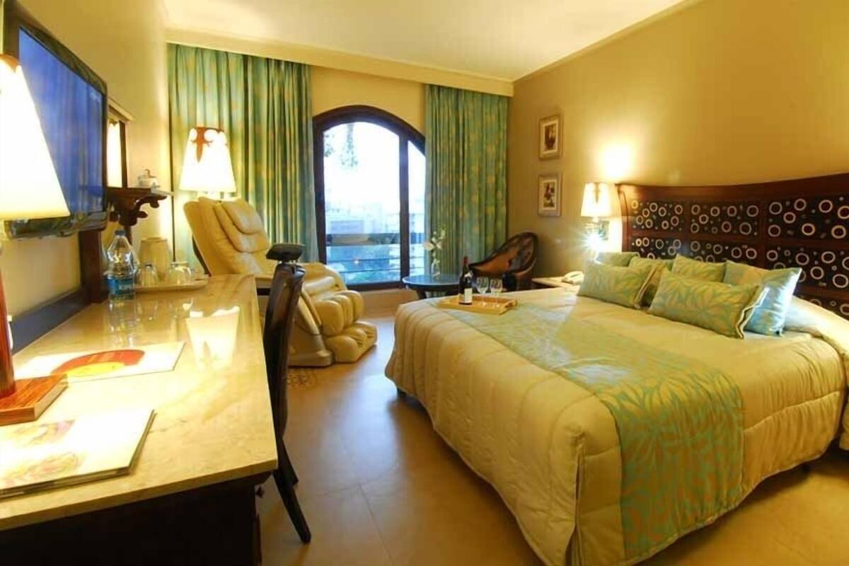 Habitación de hotel con una cama grande, un escritorio con una silla, un sillón de masaje y vistas al exterior.