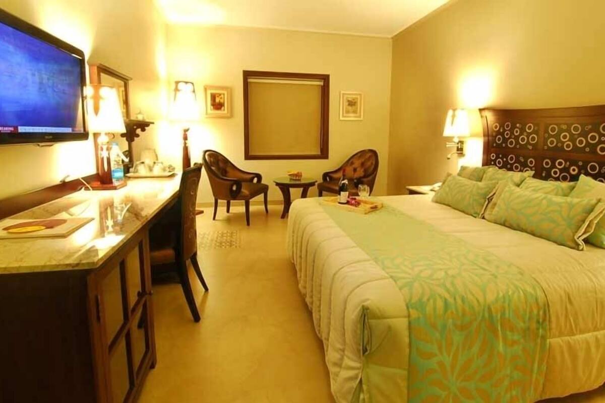 Habitación de hotel con cama, escritorio, televisión, dos sillones, una mesita y televisión montada en la pared.