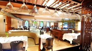 Um restaurante com várias mesas, cadeiras e luminárias pendentes.