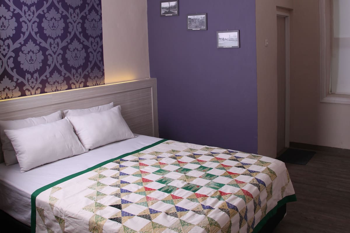 A neatly made bed with a colorful quilt, a patterned wallpaper on one wall, and a plain wall on the other.