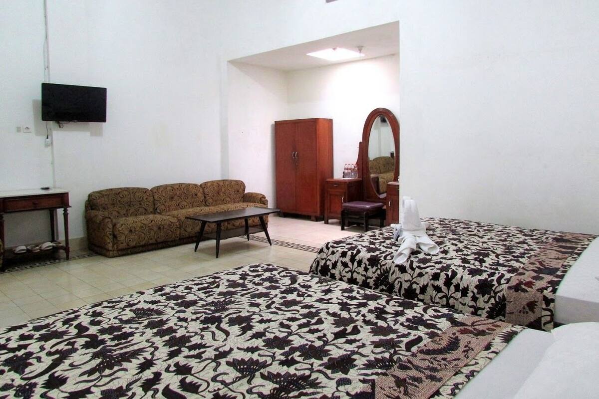 A room with a sofa, a bed with patterned bedding, a wooden cabinet, a mirror, and a television mounted on the wall.