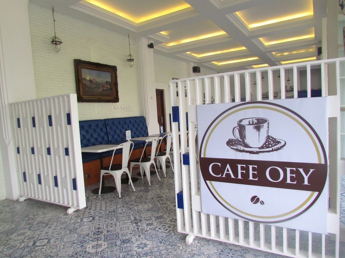 A cafe area with a sign reading "CAFE OEY," a seating area with white chairs and a blue cushioned bench, and a patterned carpet.