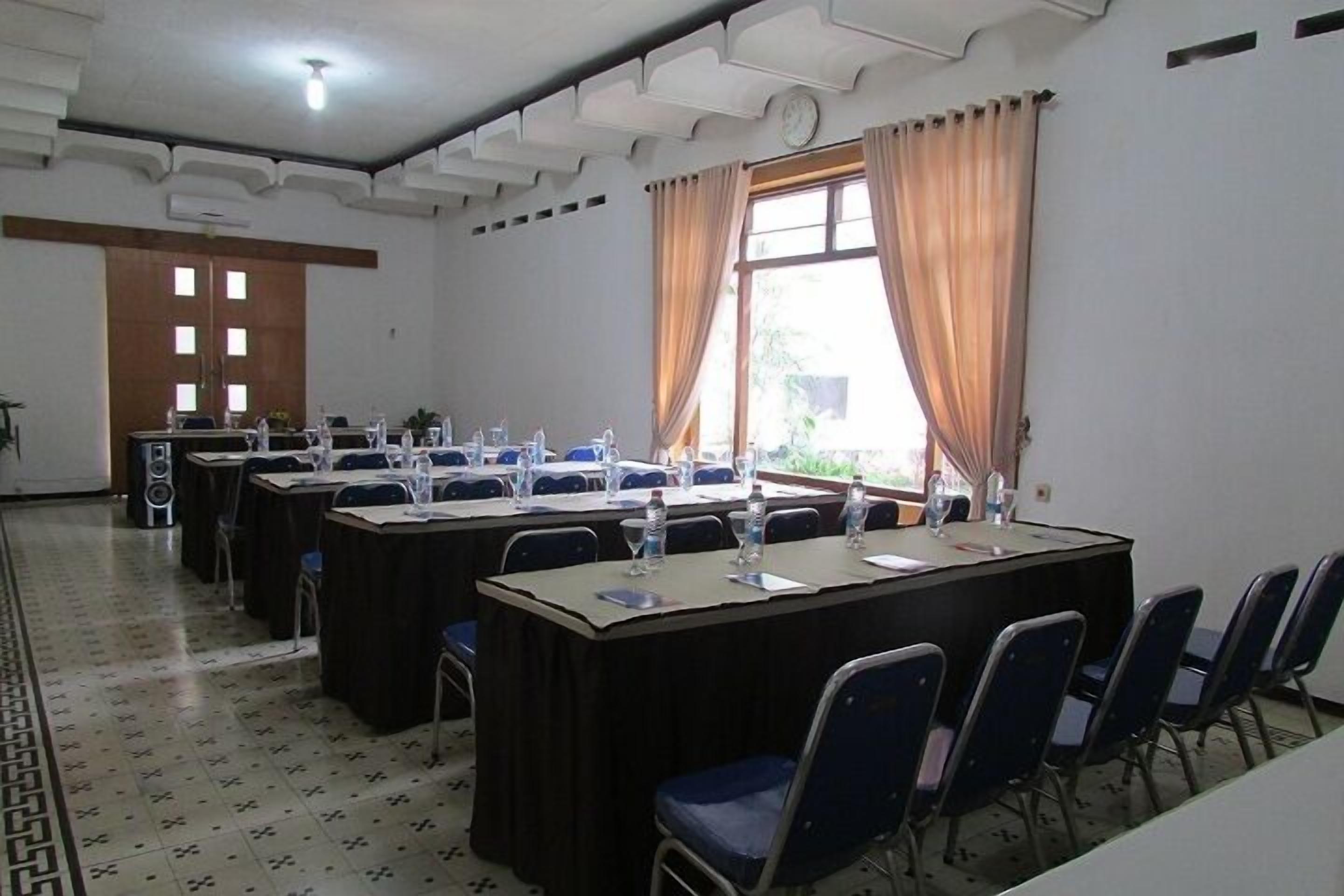 A conference room with long tables and chairs, a clock on the wall, and a window with curtains.