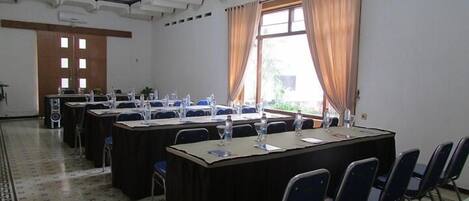 A conference room with long tables and chairs, a clock on the wall, and a window with curtains.