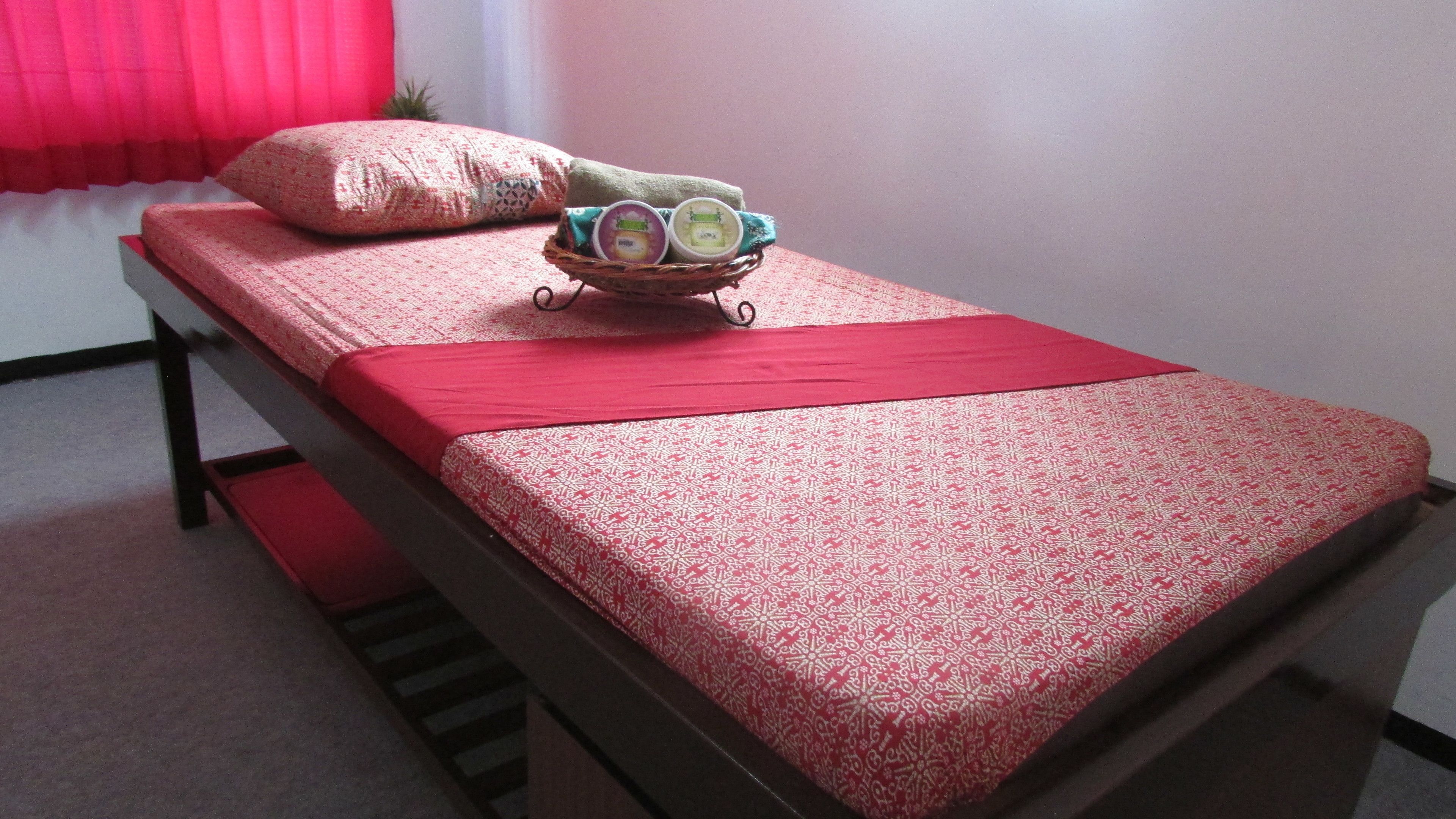 A single bed with a red bedspread and a patterned pillow. A small basket with toiletries is placed on the bed.