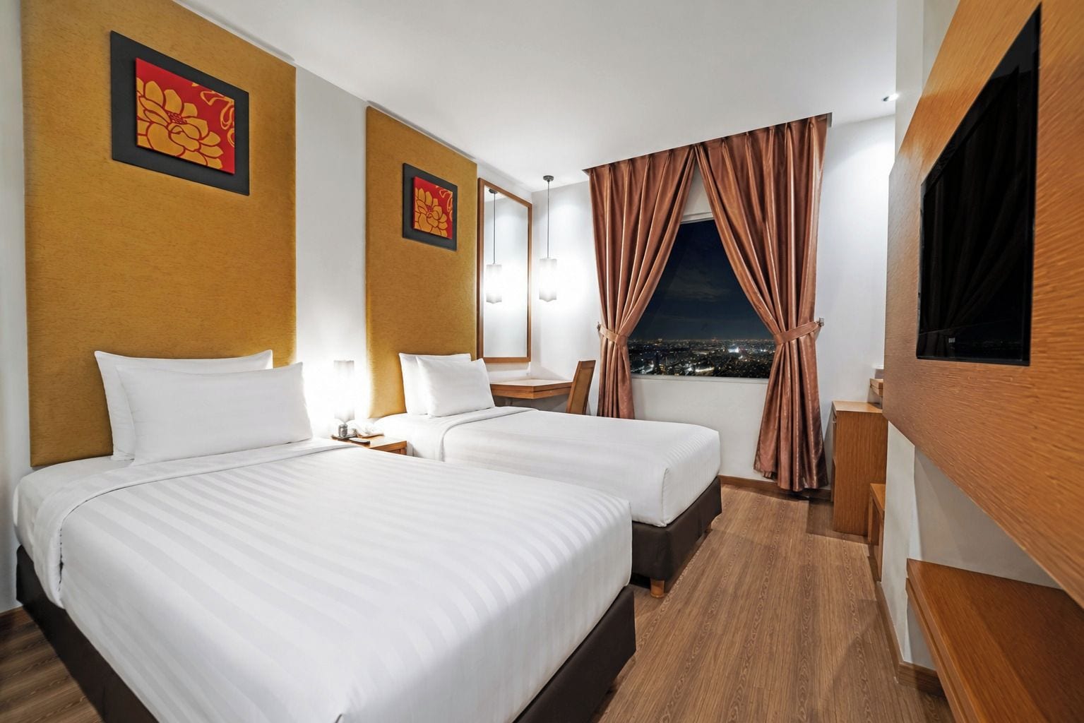 A hotel room with two beds, a desk, a chair, a TV, and a window with curtains.