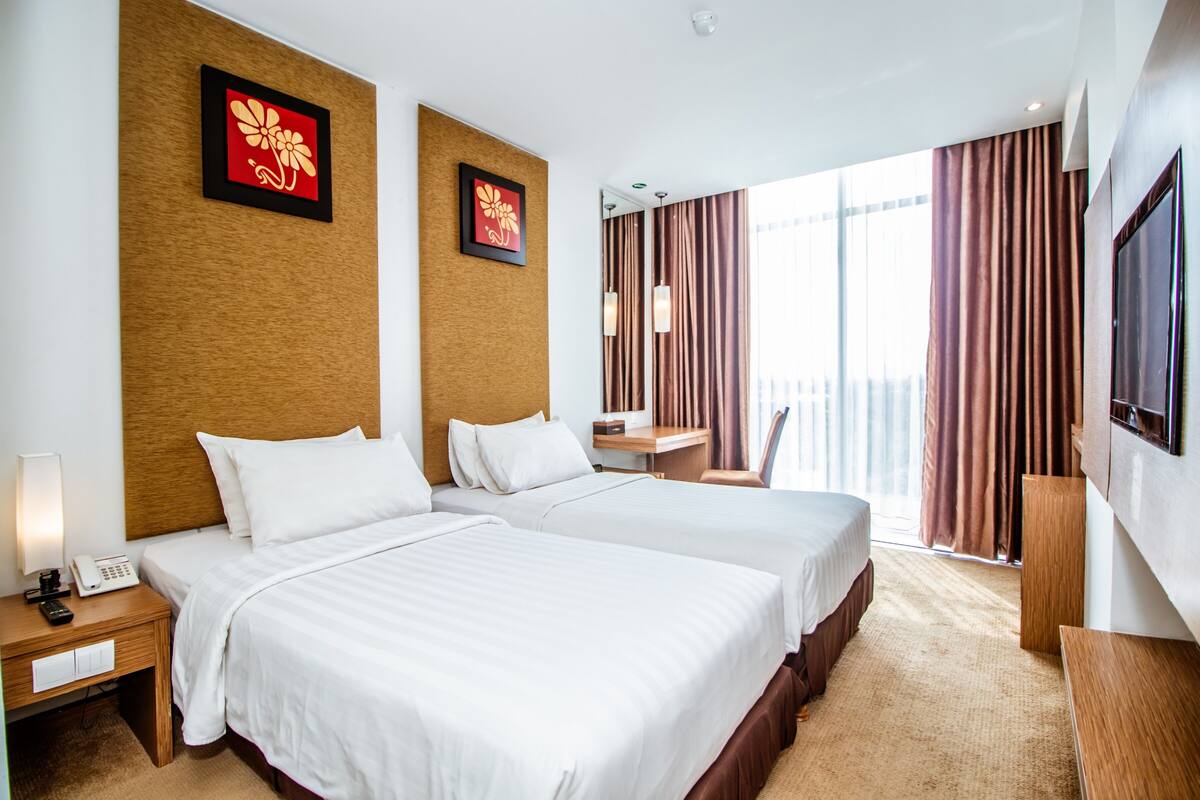 A hotel room with two beds, a desk, a chair, a TV, and a balcony with curtains.