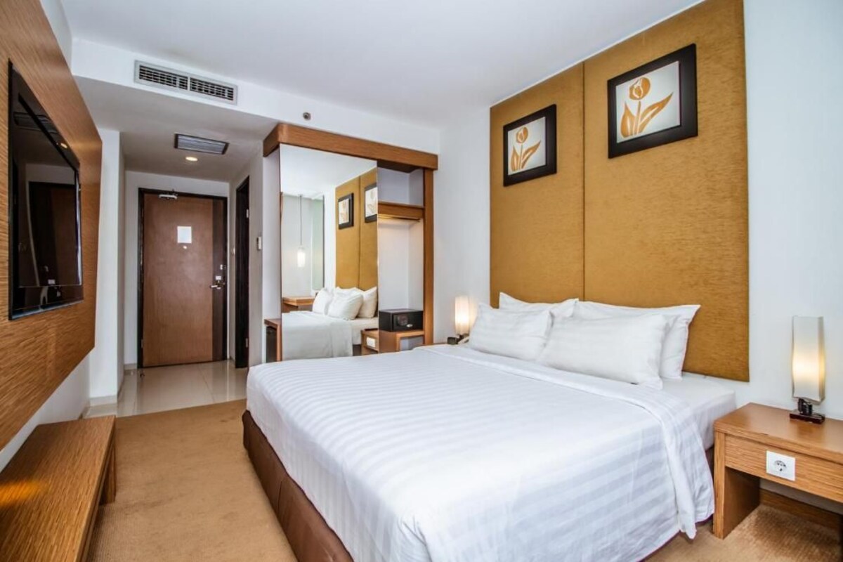 A hotel room with a large bed, bedside tables, a mirror, and a wall-mounted TV.