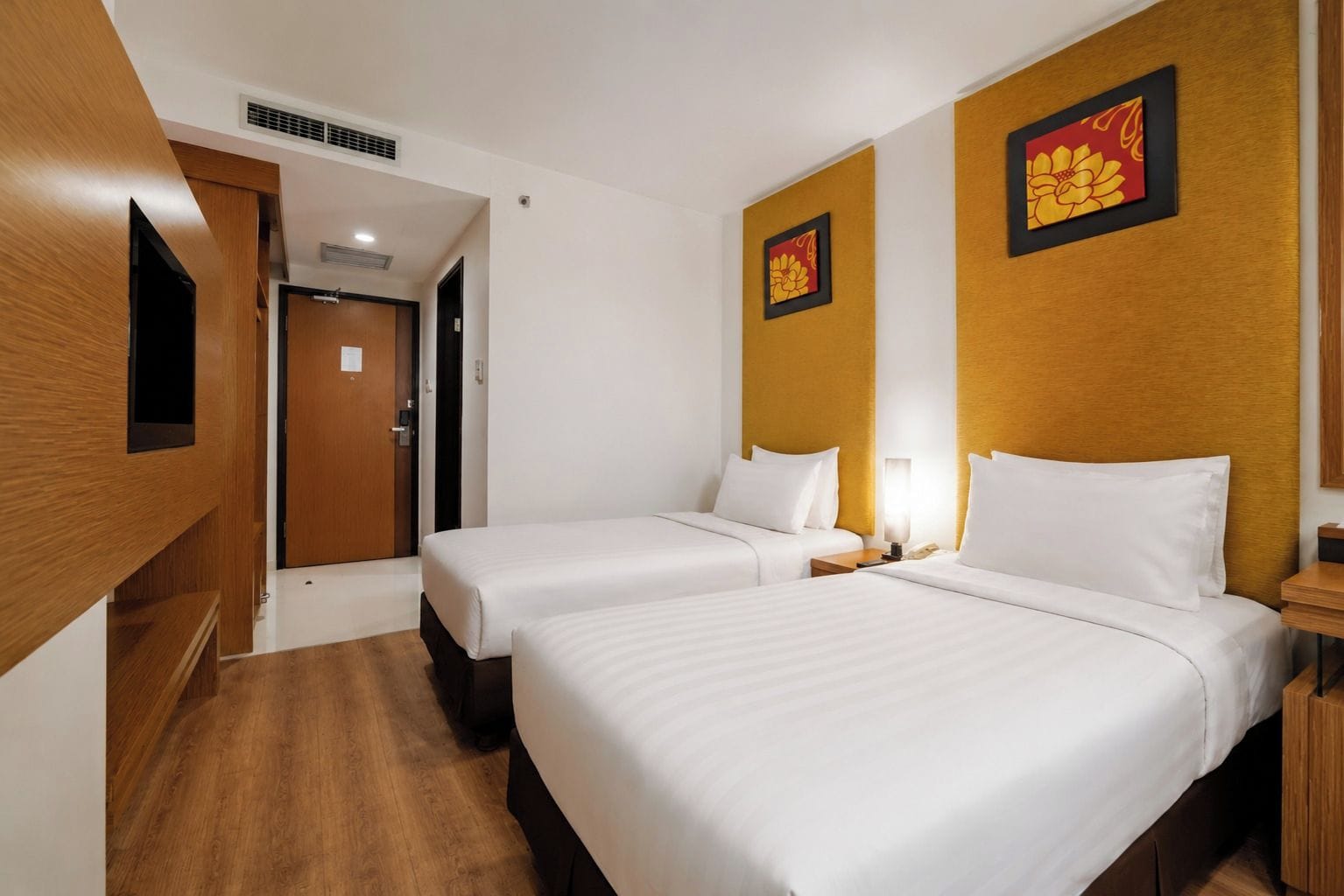 A hotel room with two beds, a wooden wardrobe, and two wall-mounted artwork pieces.