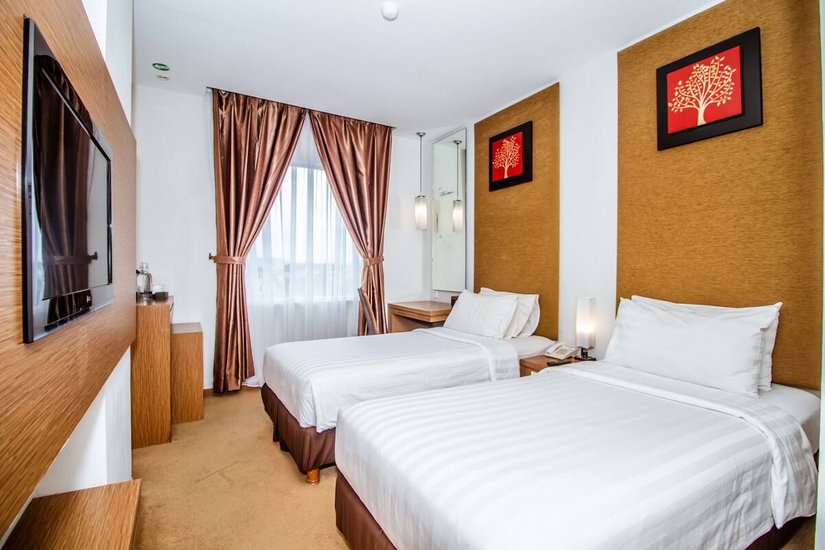 A hotel room with two beds, a TV, a desk, and a window with curtains.