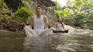 Two individuals meditating in a natural setting with a stone structure and greenery in the background. - Joglo Plawang Boutique Villa (Pakem)