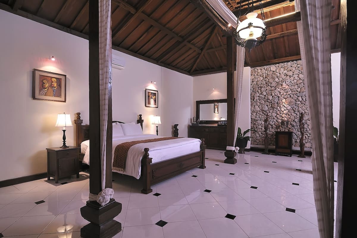 A hotel room with a large bed, two bedside tables with lamps, a stone wall, and a ceiling with wooden beams.