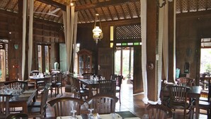 A spacious dining area with wooden tables and chairs, a high ceiling with patterned beams, and a hanging light fixture. - Joglo Plawang Boutique Villa (Pakem)