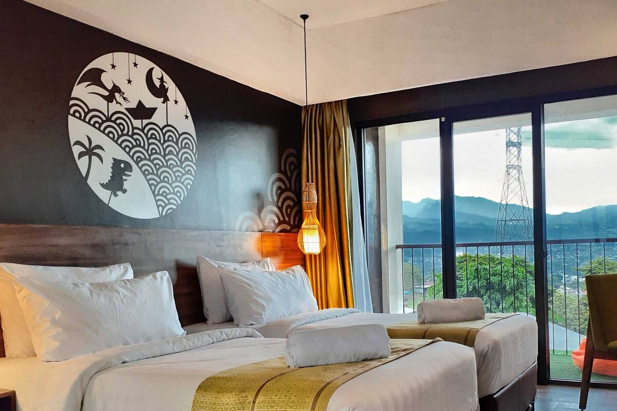 Une chambre d’hôtel avec deux lits, une grande fenêtre donnant sur les montagnes et une fresque murale décorative.