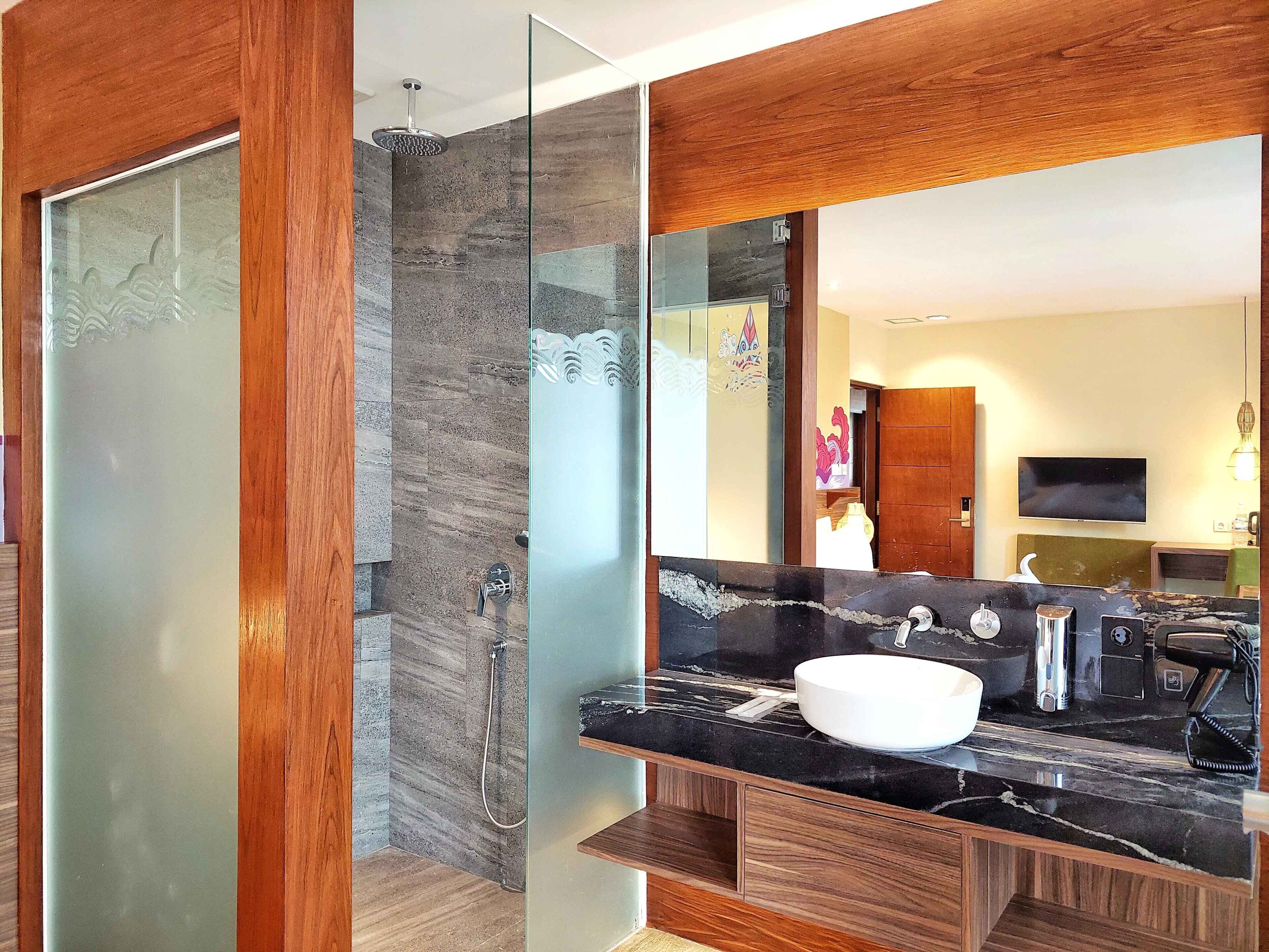 Un baño moderno con cabina de ducha de vidrio, lavamanos de mármol negro y muebles de madera.