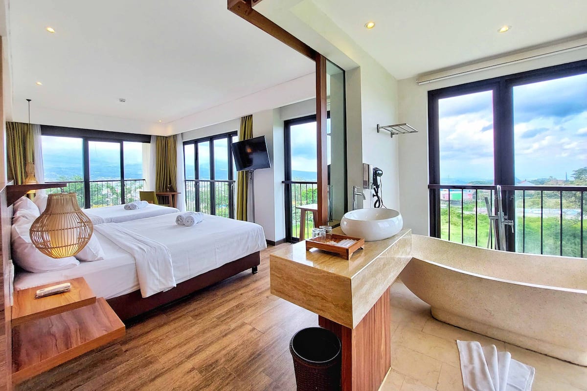 Une chambre d’hôtel avec deux lits, une grande fenêtre, une télévision, un lavabo et un balcon avec vue.