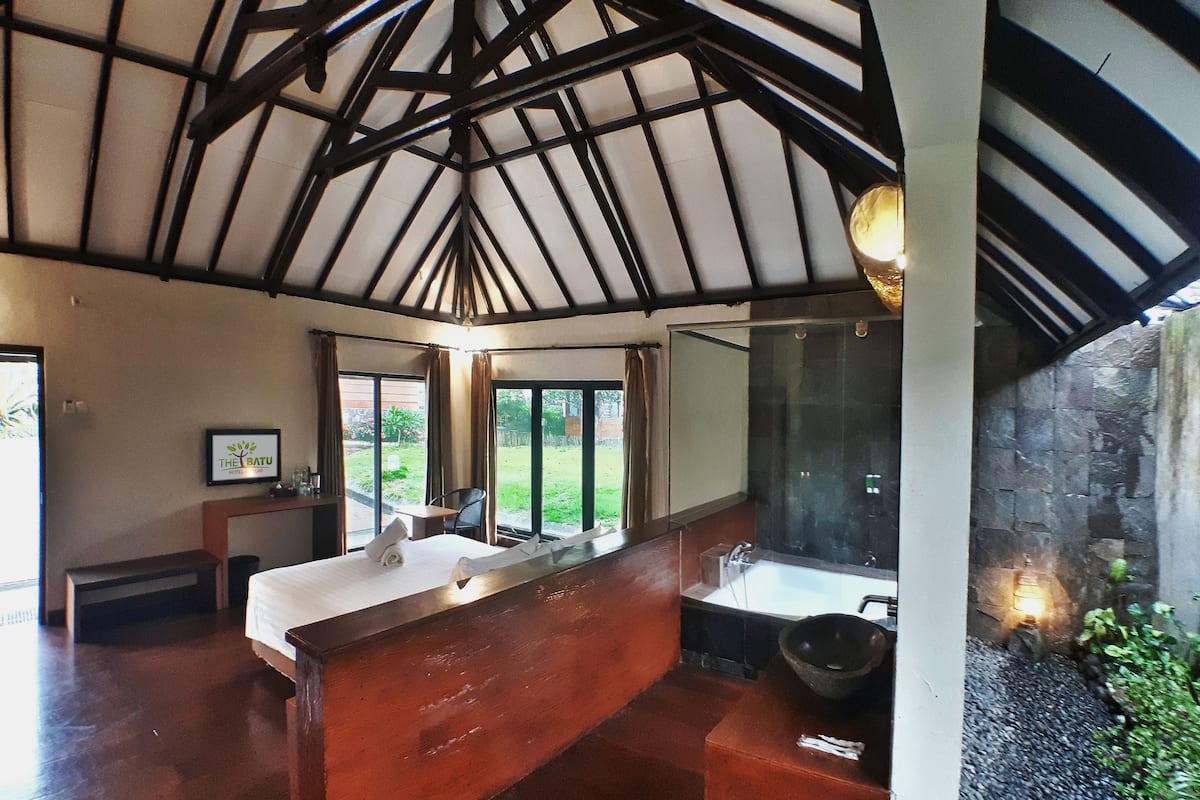 Une salle de bain d’hôtel avec un meuble-lavabo en bois, un grand miroir et un mur en pierre.