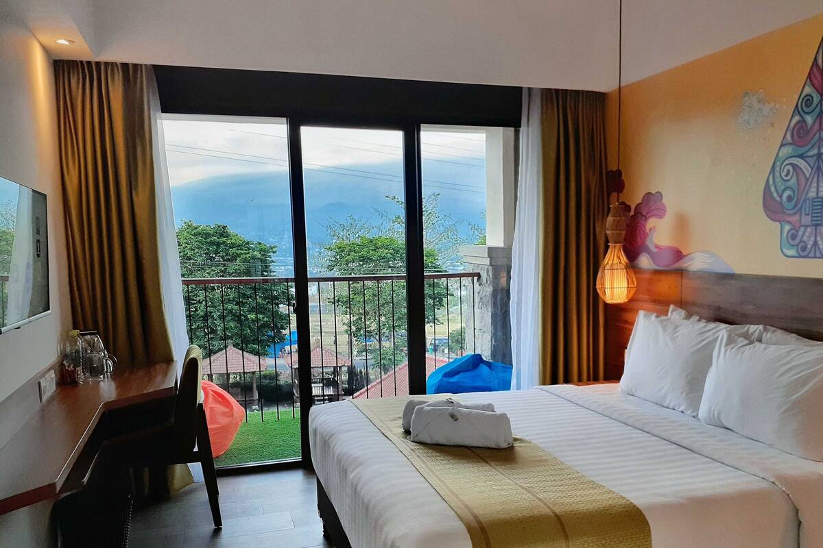 Une chambre d’hôtel comprenant un lit, un bureau, une chaise, un balcon avec vue et un élément décoratif mural.
