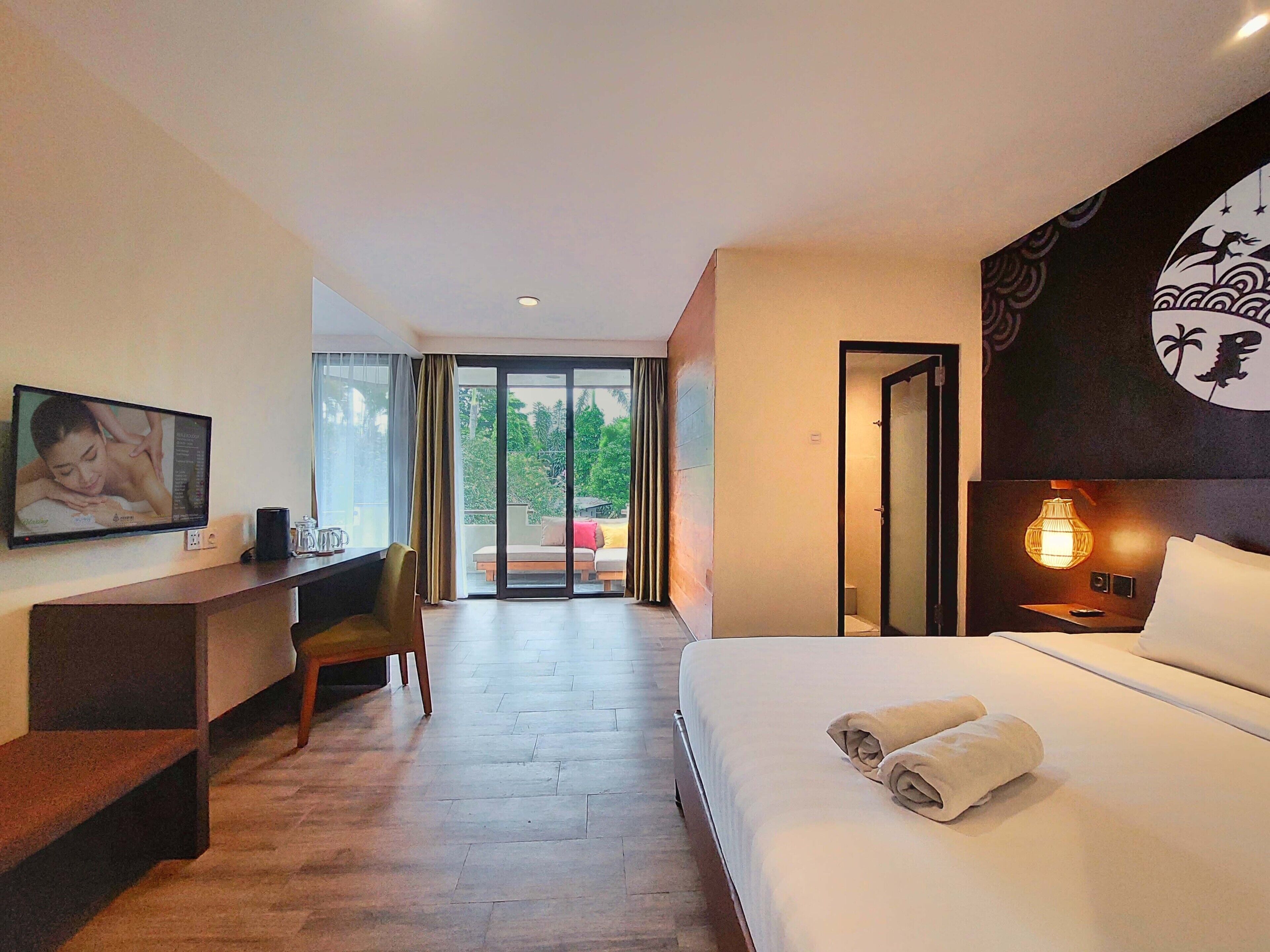 Habitación de hotel con cama, escritorio, silla, televisión y vistas al exterior.