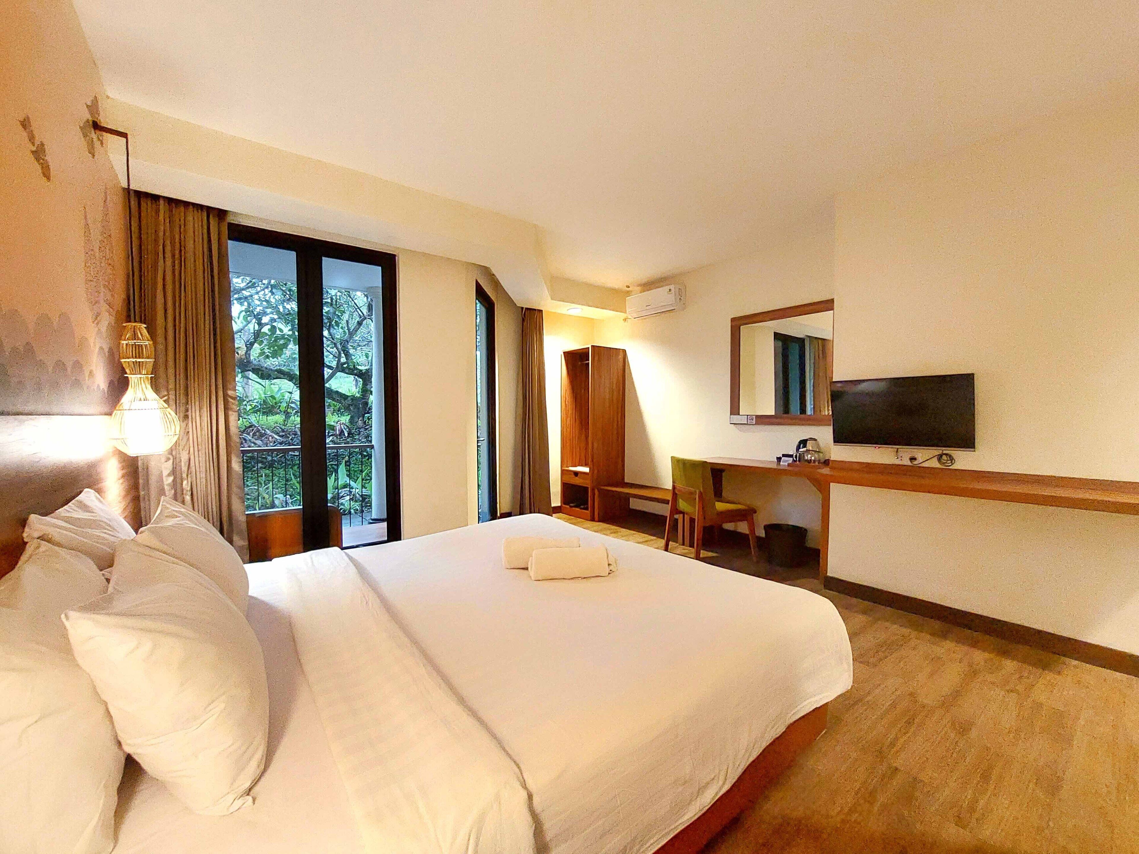 Camera d'albergo con un letto grande, una scrivania, una sedia, una TV e vista su spazi verdi.