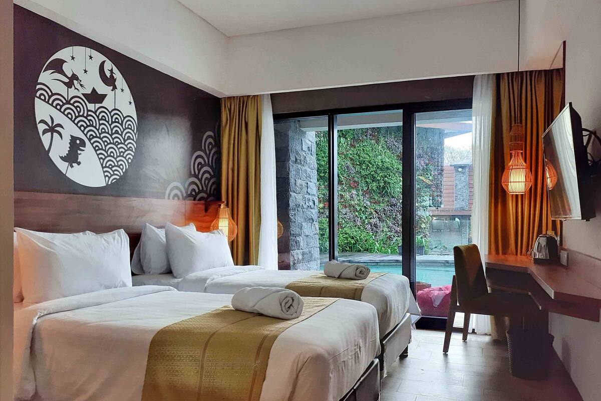 Une chambre d’hôtel avec deux lits, un bureau, une télévision et une grande fenêtre donnant sur un paysage verdoyant.