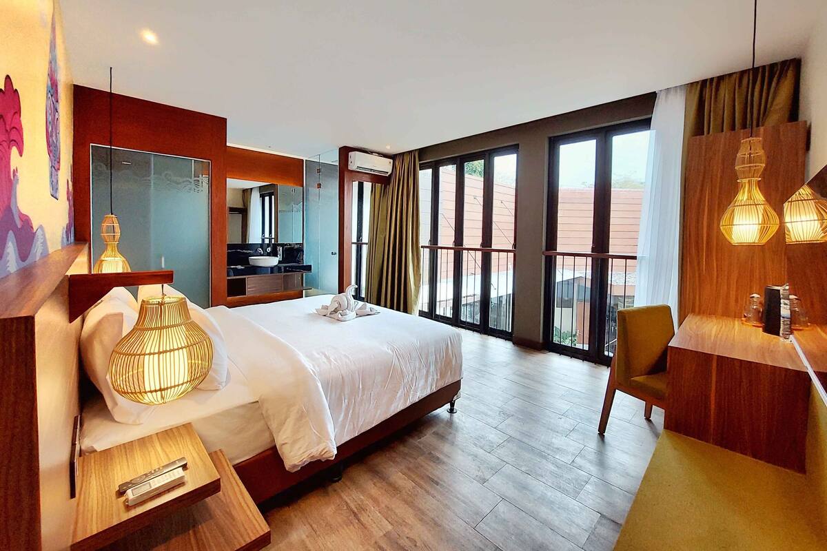 Une chambre d’hôtel moderne dotée d’un grand lit, d’une salle de bain avec une douche en verre et d’un balcon offrant une vue agréable.