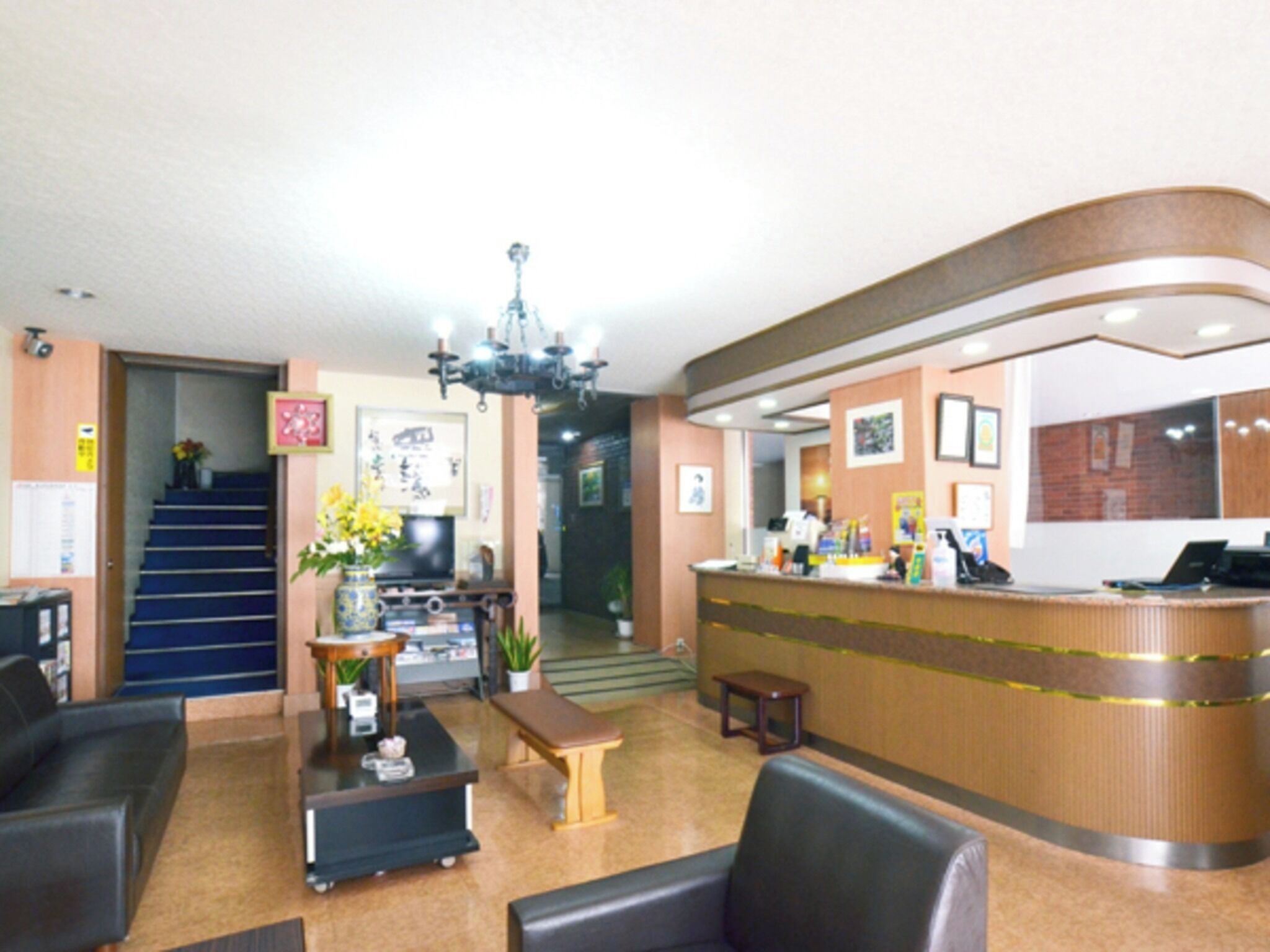 A hotel lobby with a reception desk, seating area, staircase, and a chandelier.